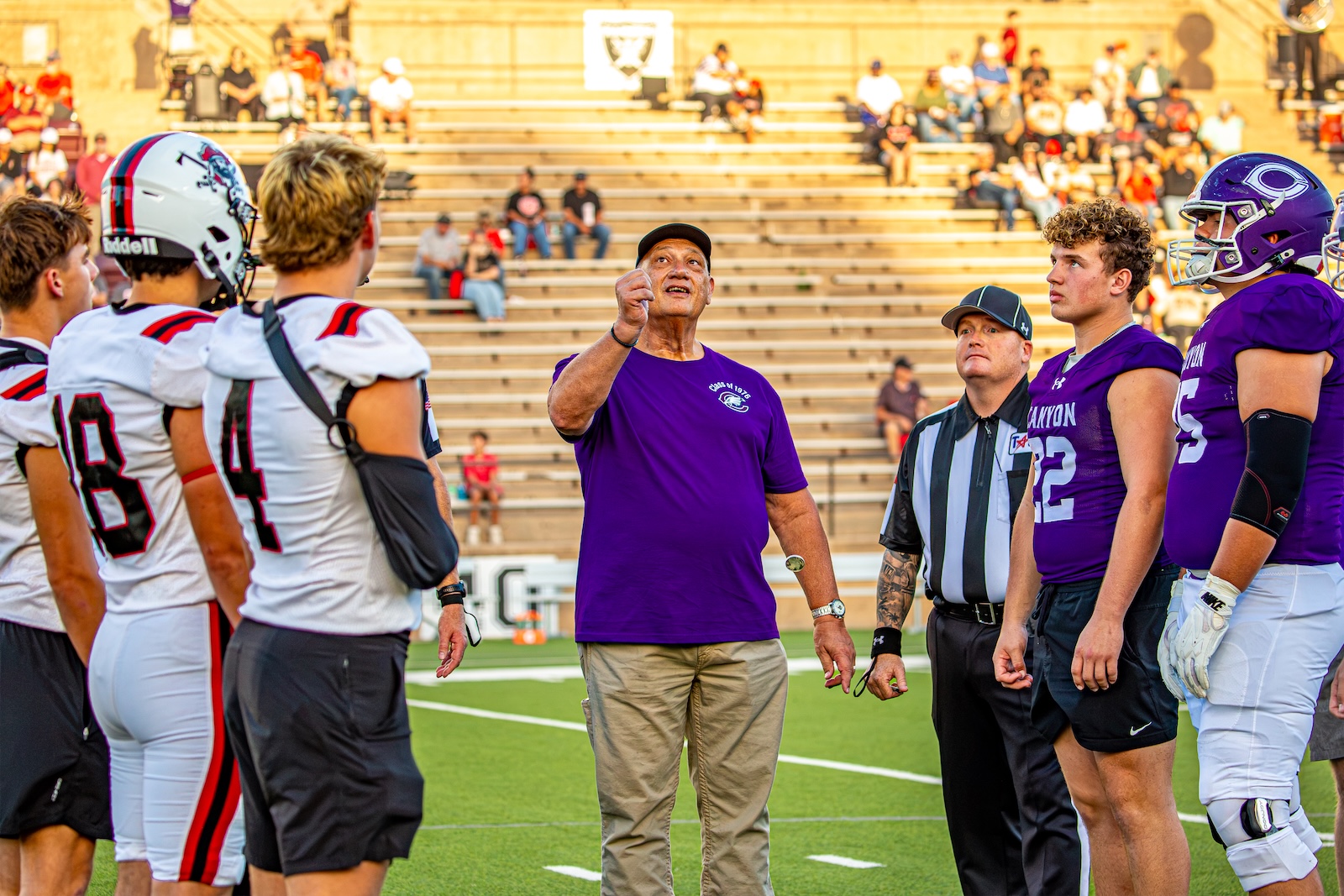 _V4A2700 | Press Pass Sports Football coach in a purple shirt gesturing to players as a referee watches on the field before kickoff.