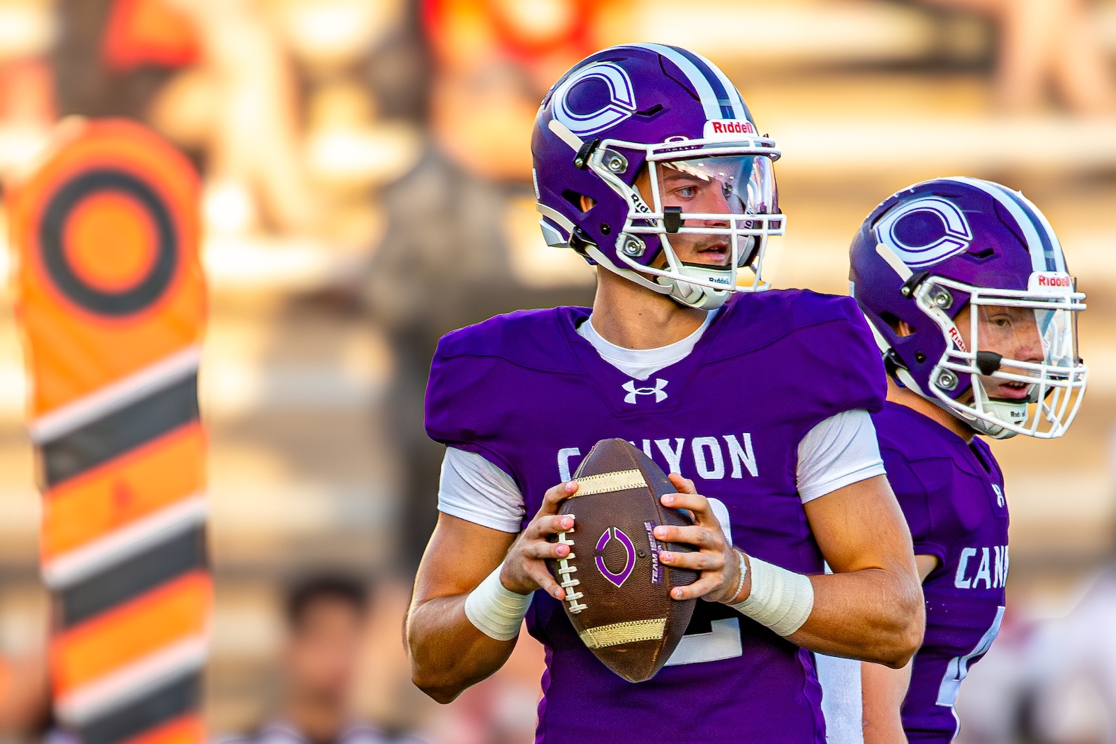 _V4A2739 | Press Pass Sports Two football players in purple Canyon uniforms, one quarterback holding a ball and looking to throw on the field.