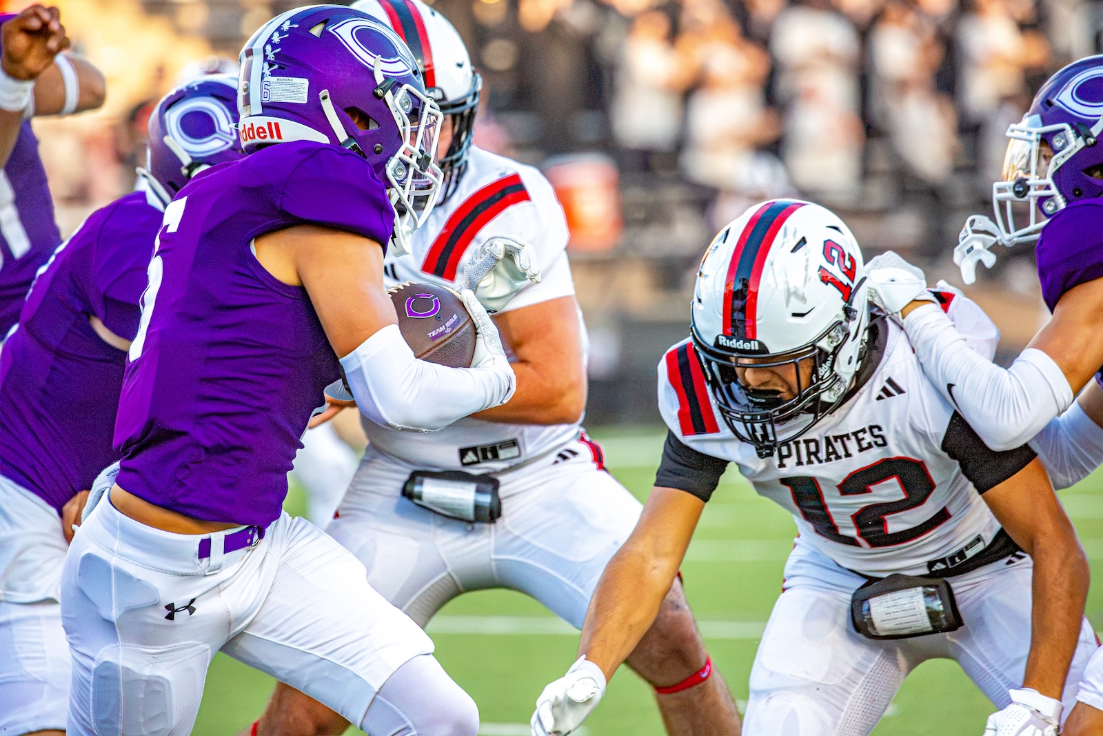 _V4A2747 | Press Pass Sports Football player in a purple jersey carries the ball as defenders in white converge on him on the field