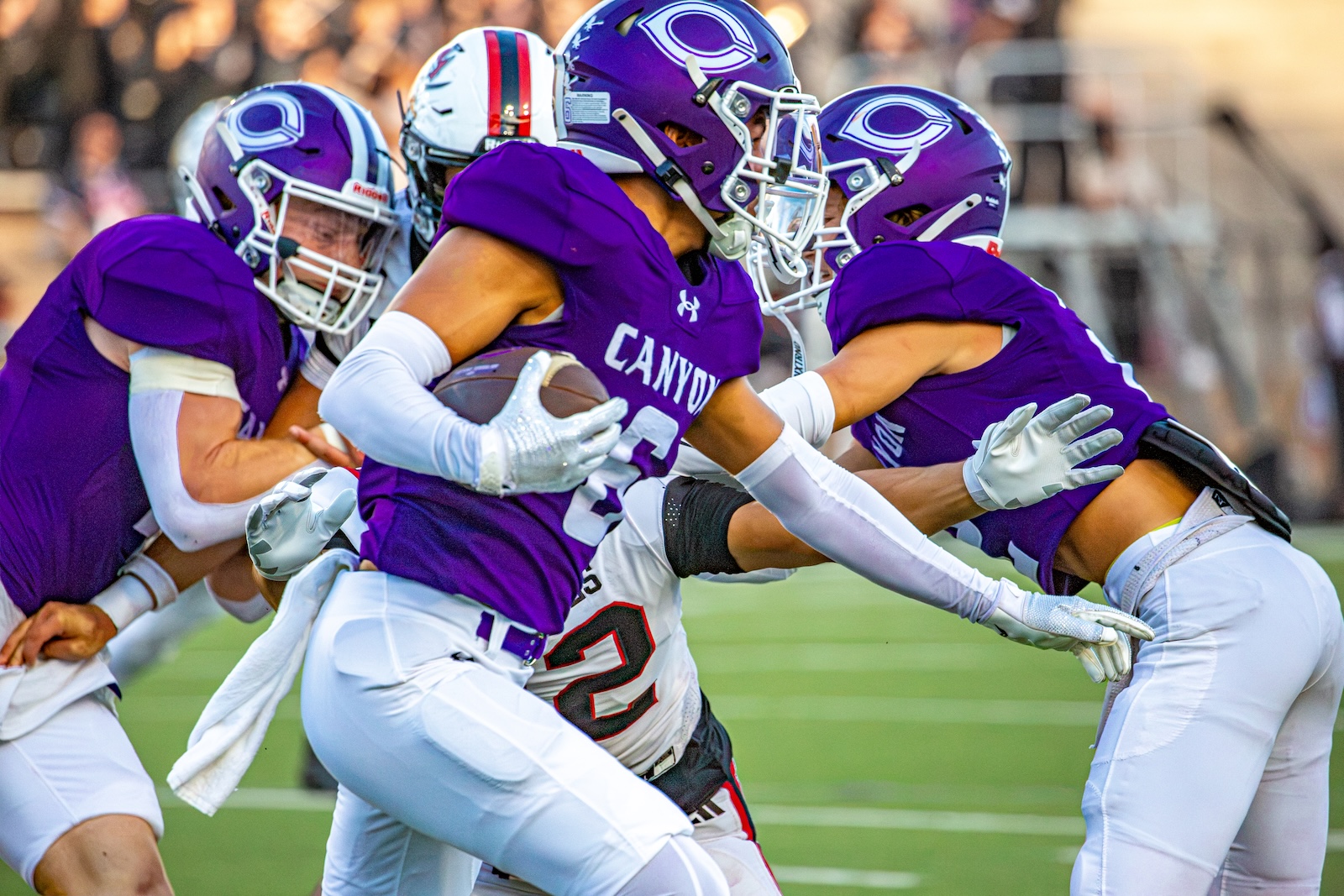 _V4A2748 | Press Pass Sports Football players in purple jerseys tackle a ball carrier on a sunny football field.