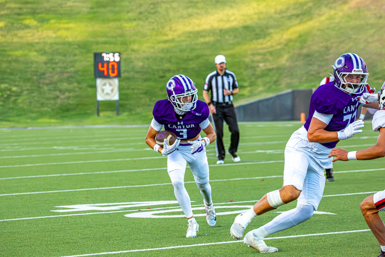 _V4A2777 | Press Pass Sports Football game scene: running back in a purple jersey (#3) carries the ball while sprinting down the field with a defender closing in nearby.
