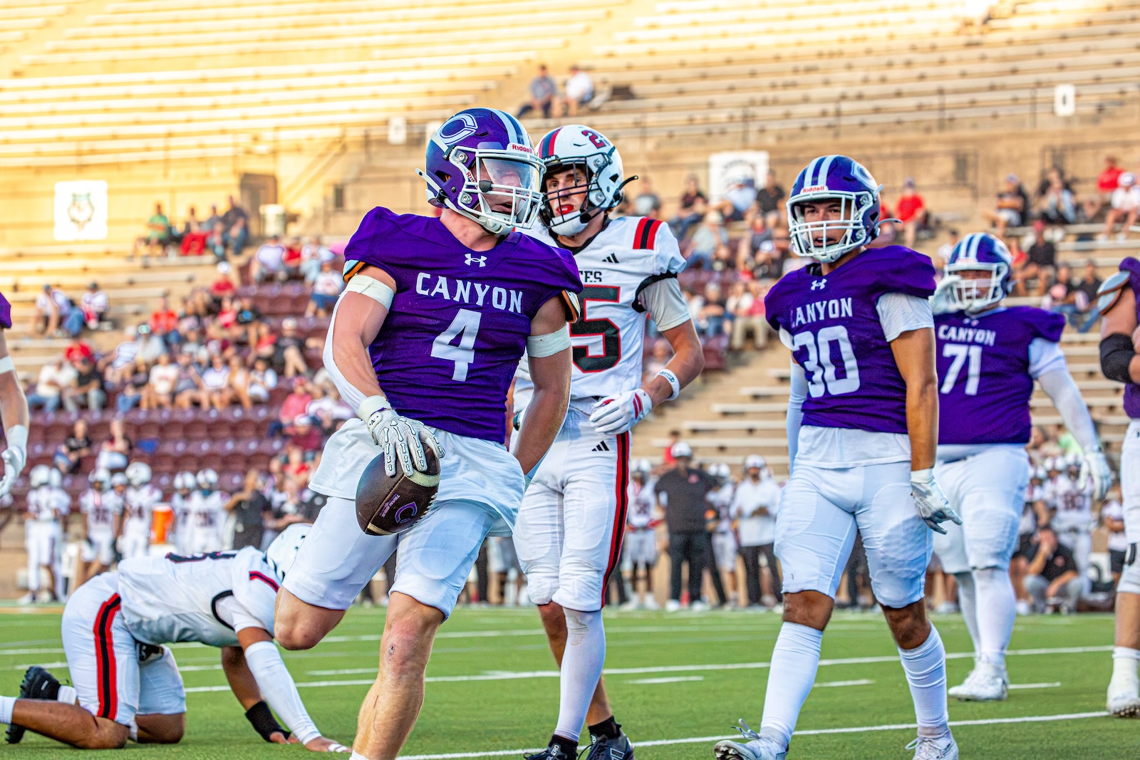 _V4A2811 | Press Pass Sports Canyon football player #4 carries the ball while advancing on the field as teammates and an opponent chase nearby.