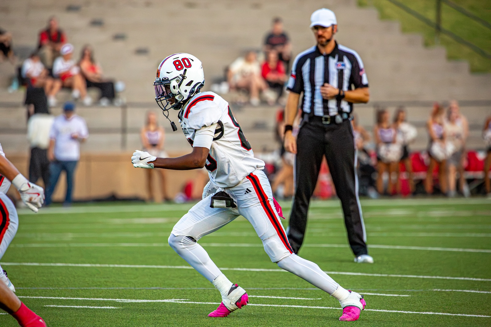 _V4A2876 | Press Pass Sports Football player in white uniform #80 sprinting on a green football field with a referee watching in the background