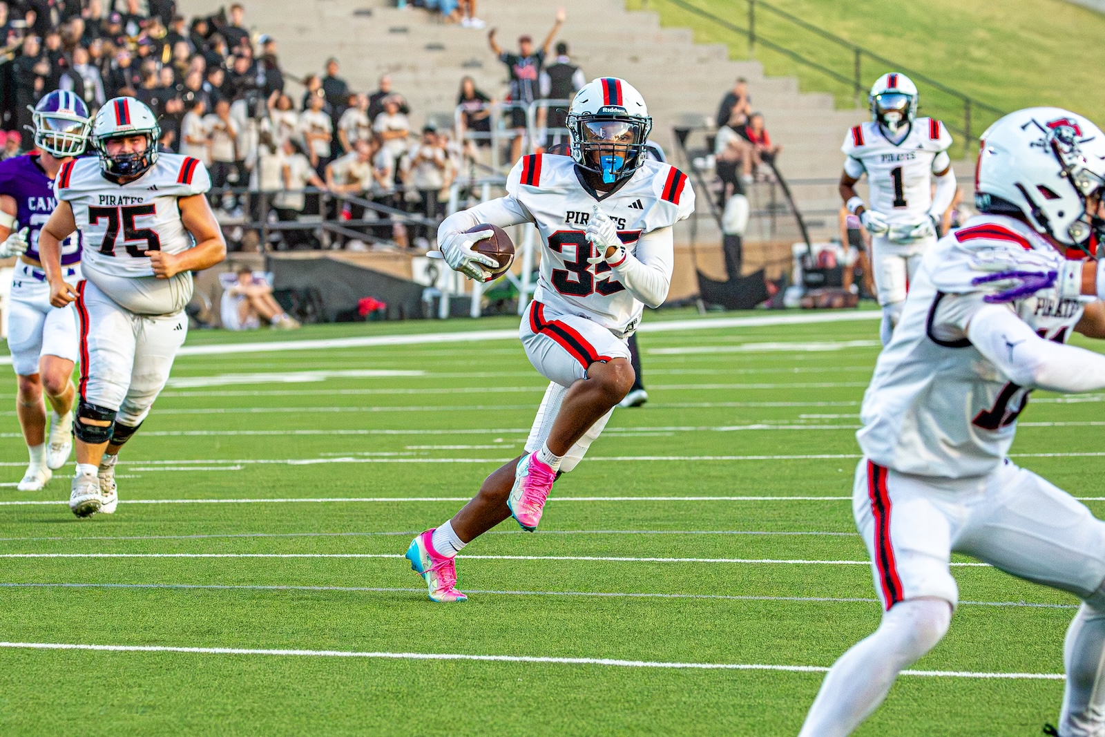 _V4A2897 | Press Pass Sports Football player (#32) in white Pirates uniform sprints with ball on a green field during a game, pink shoes visible.