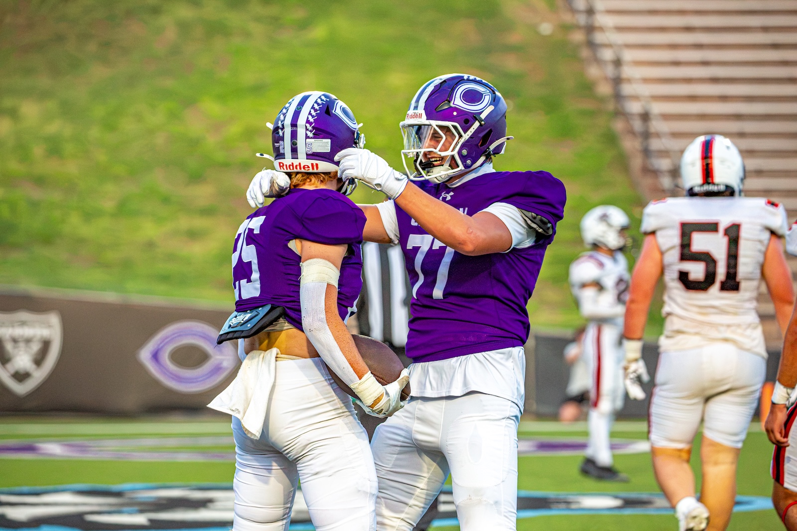 _V4A2978 | Press Pass Sports Two football players in purple uniforms embrace in a celebratory hug on the field during a game.