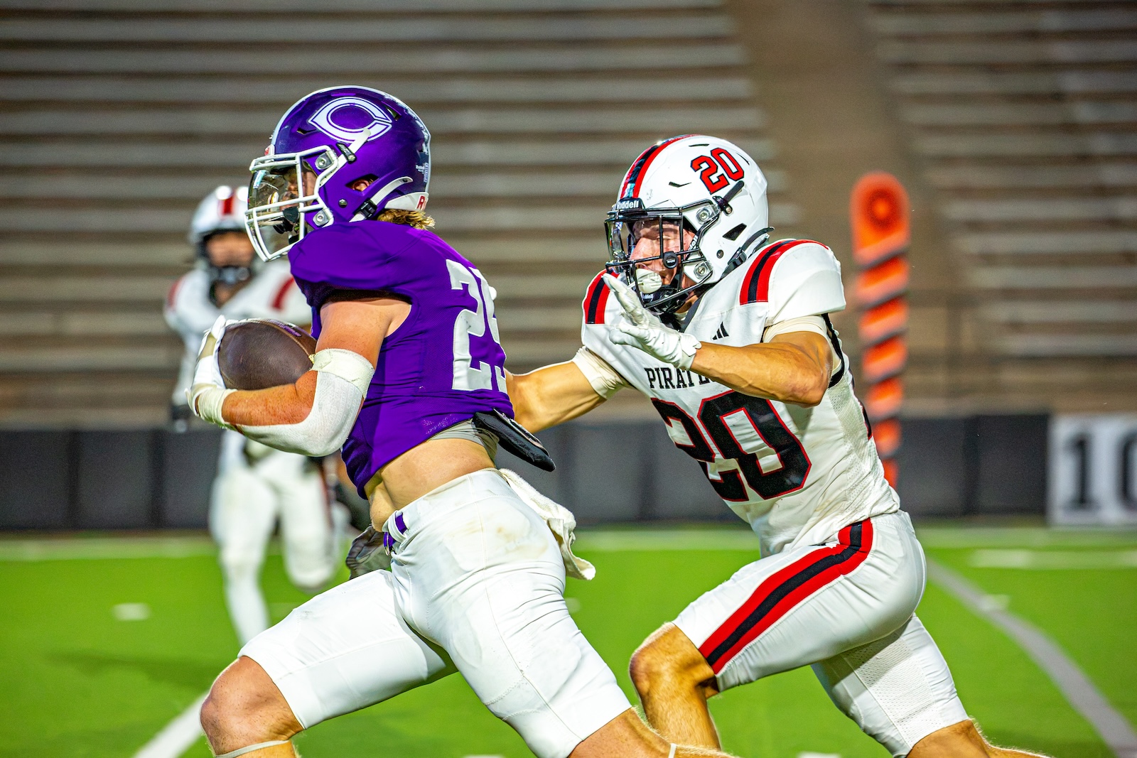 _V4A3260 | Press Pass Sports A football player in purple with the ball dodges a tackler in white and red on a green field during a game.