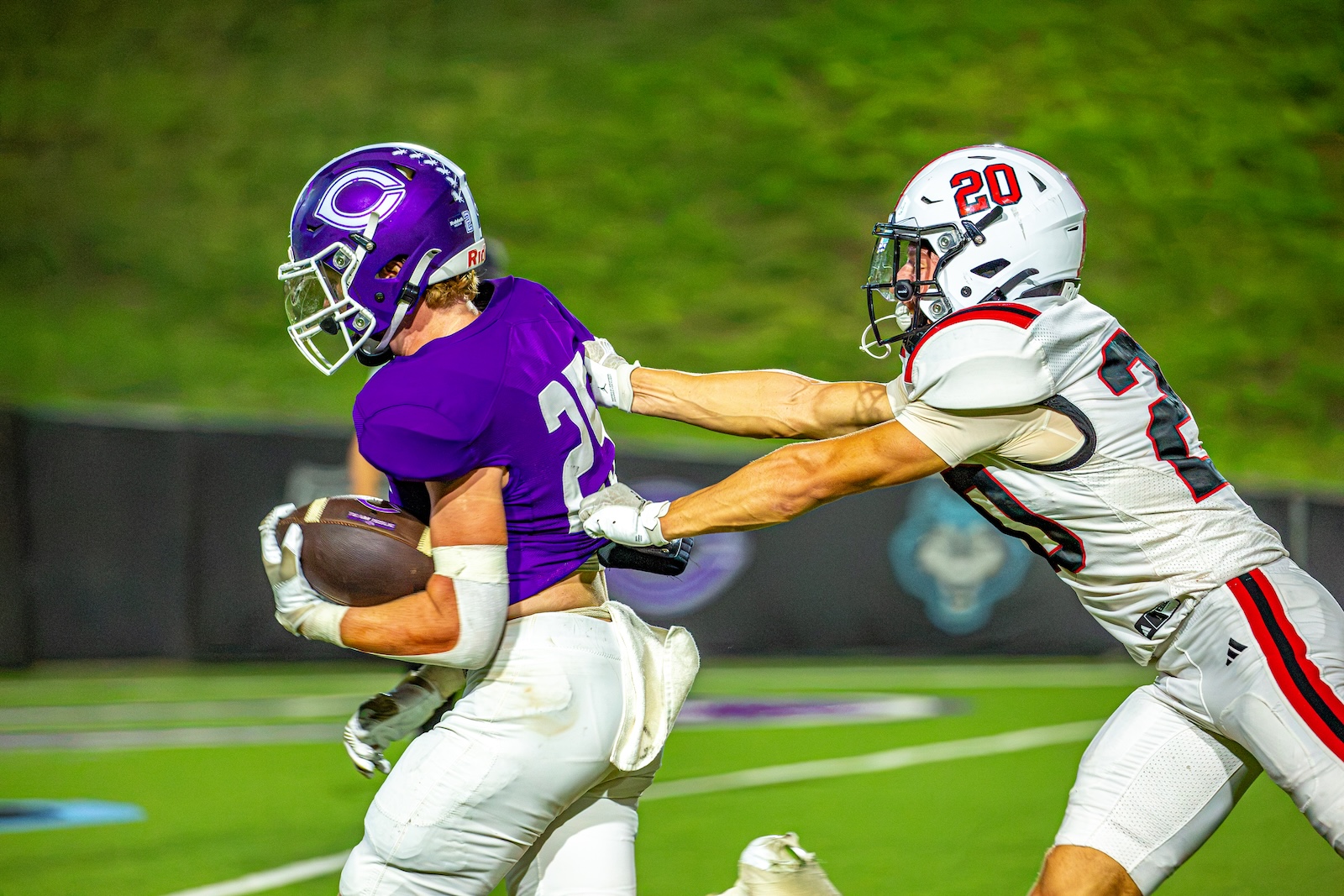 _V4A3262 | Press Pass Sports Football game: running back in purple jersey with ball, pursued by a tackler in white on a green field.
