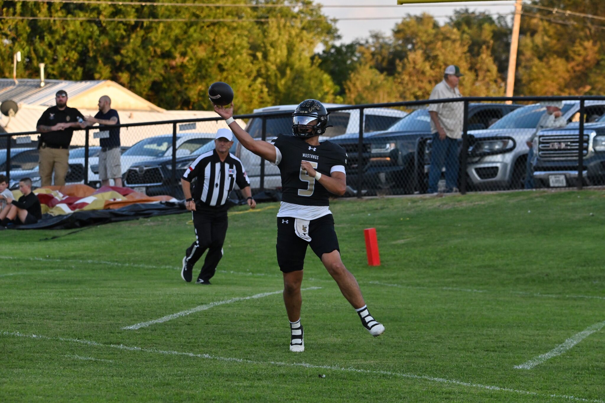 image0 35 | Press Pass Sports Football quarterback in a black jersey (number 5) throws a pass on a grassy field during a game, with referees and spectators in the background.