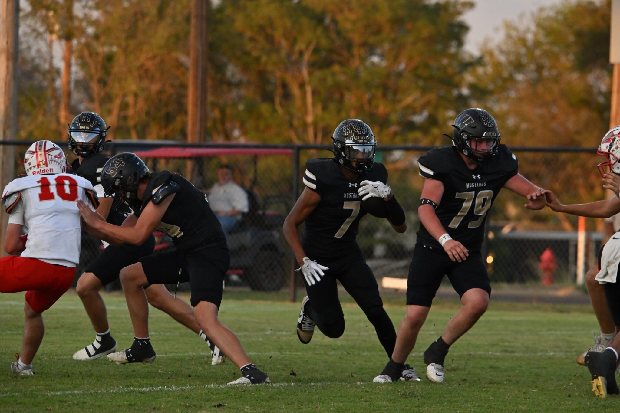 image1 27 | Press Pass Sports Football game in progress: players in black Mustangs uniforms clash with a white and red team at the line of scrimmage on a grassy field.