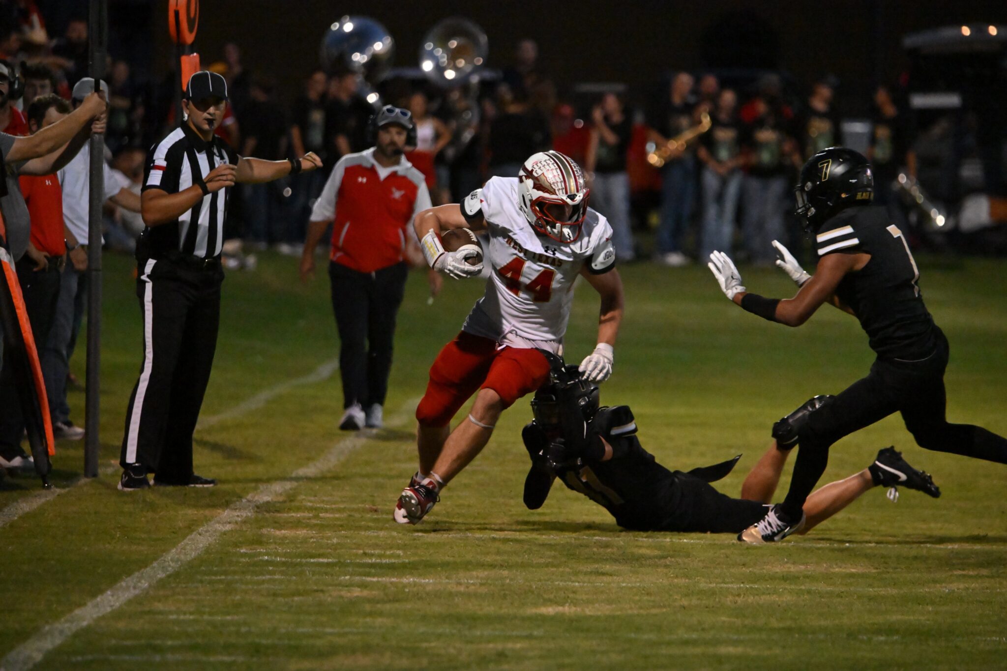 image2 13 | Press Pass Sports Nighttime football action: ball carrier in white and red runs along the sideline as a defender lunges nearby with a crowd in the background.