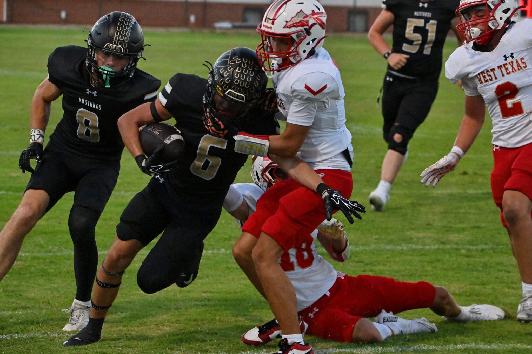 image2 14 | Press Pass Sports White-jersey West Texas defender wraps up a black-uniformed ball carrier during a brisk football play on a grassy field.