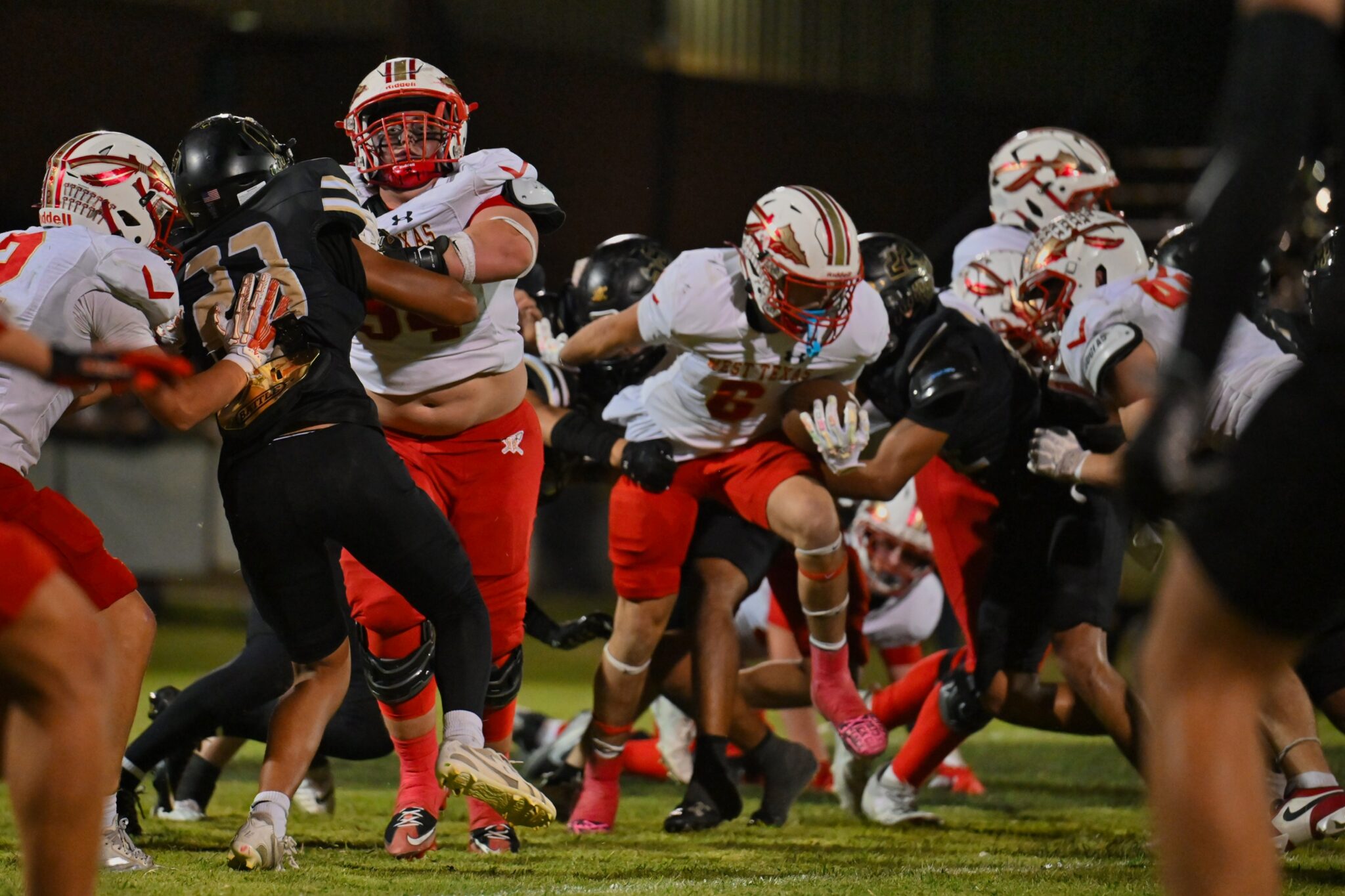 image3 12 | Press Pass Sports High-action football game: white-and-red team tackles a black-jersey runner on a grassy field at night.