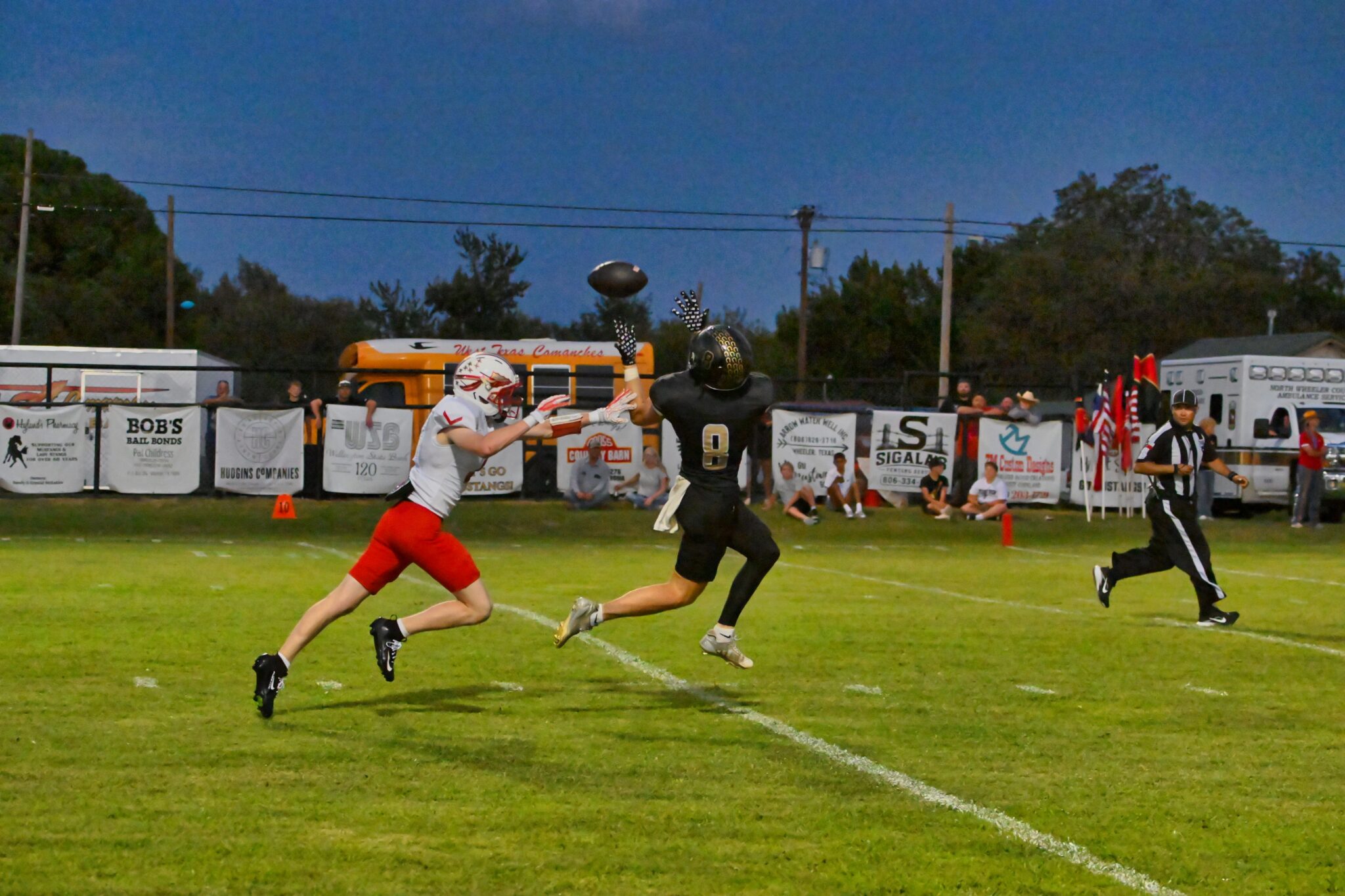 image6 9 | Press Pass Sports Two football players leap for a mid-air catch near the sideline as banners and spectators watch from the sidelines.