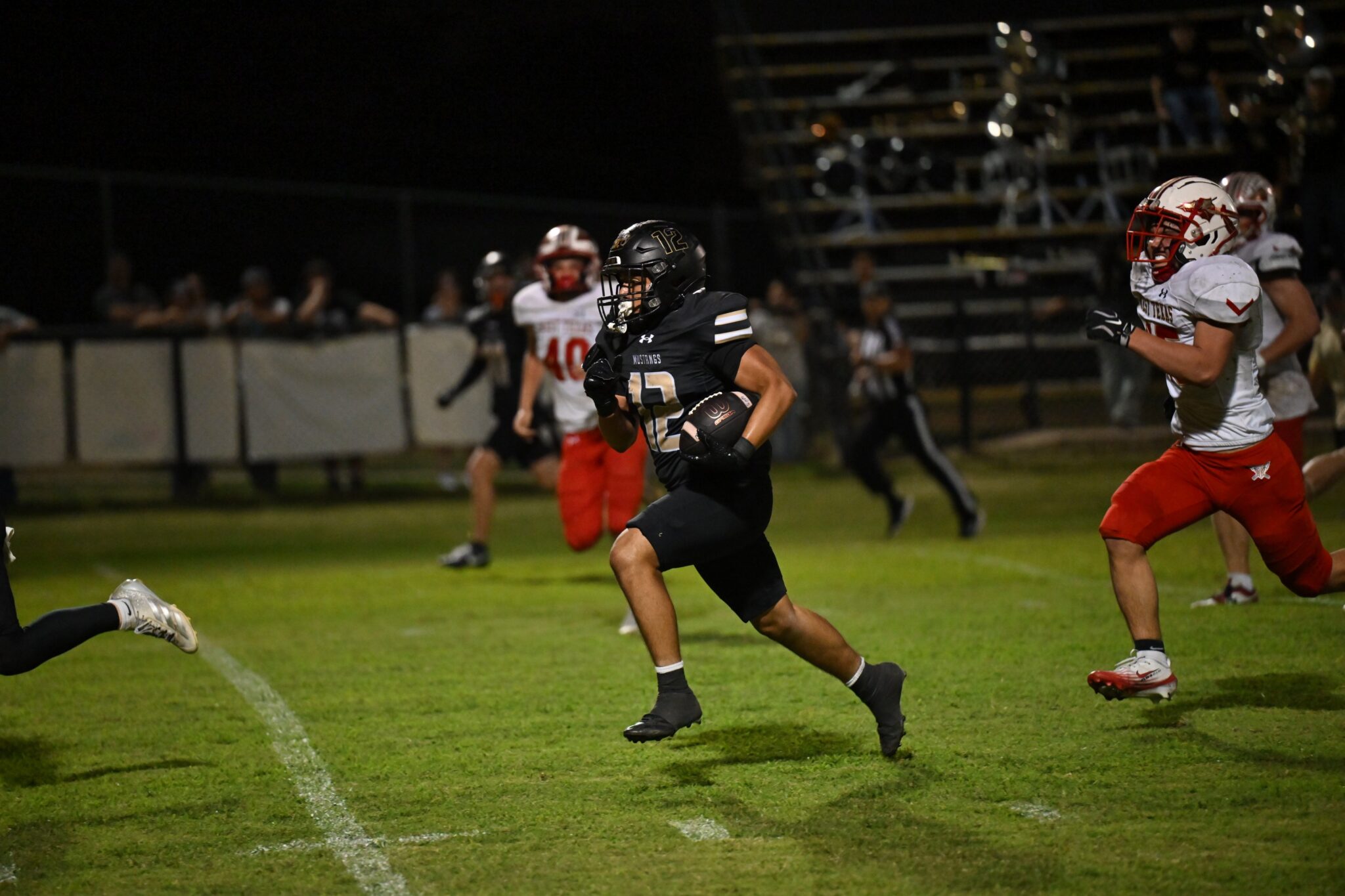 image8 5 | Press Pass Sports Nighttime football action: a running back in a black uniform (number 13) carries the ball down the field as defenders in white and red close in.