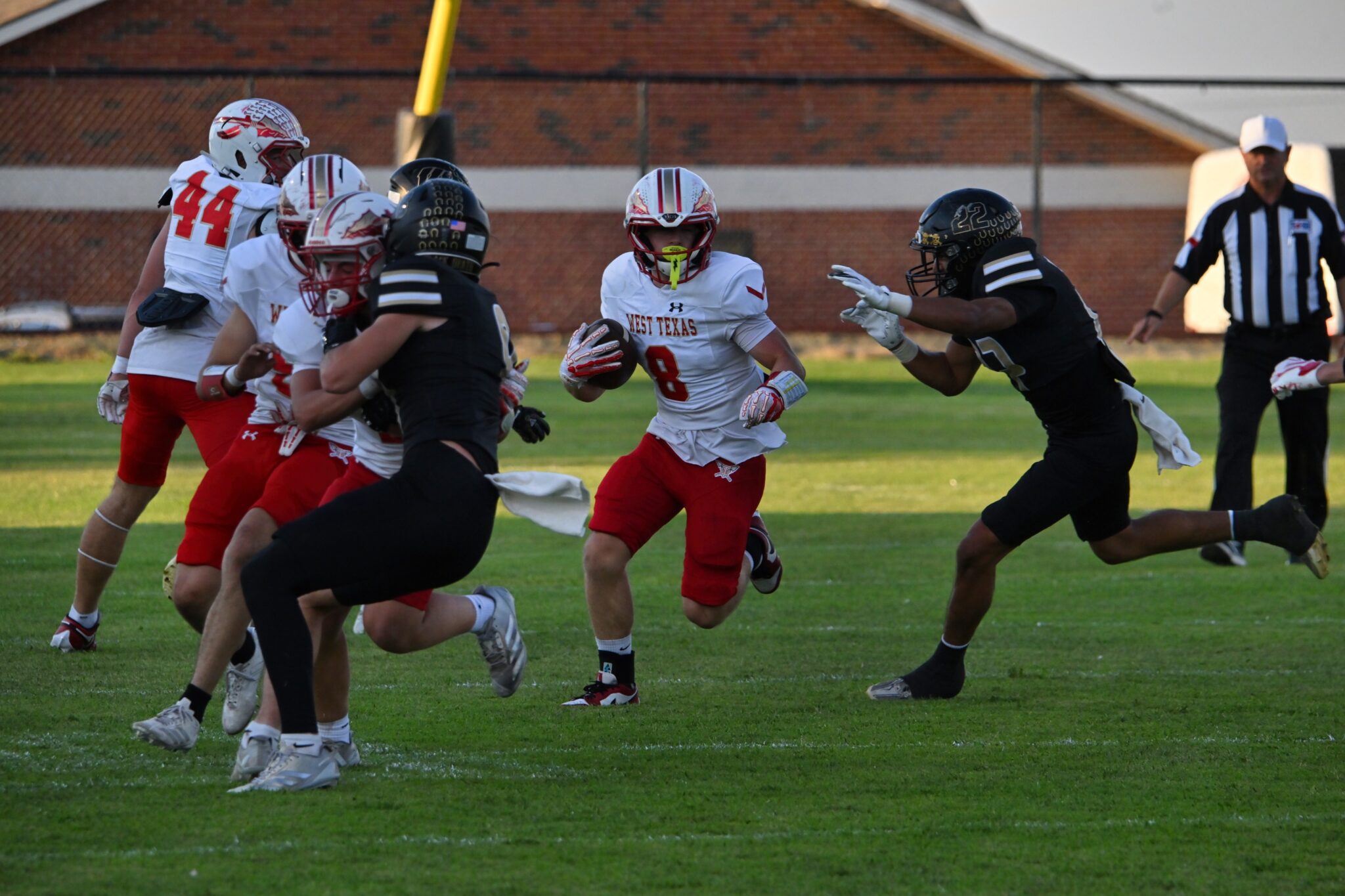image10 1 | Press Pass Sports Football game moment: a player in a white West Texas jersey runs with the ball while a black-uniform defender closes in, with a referee in the background.