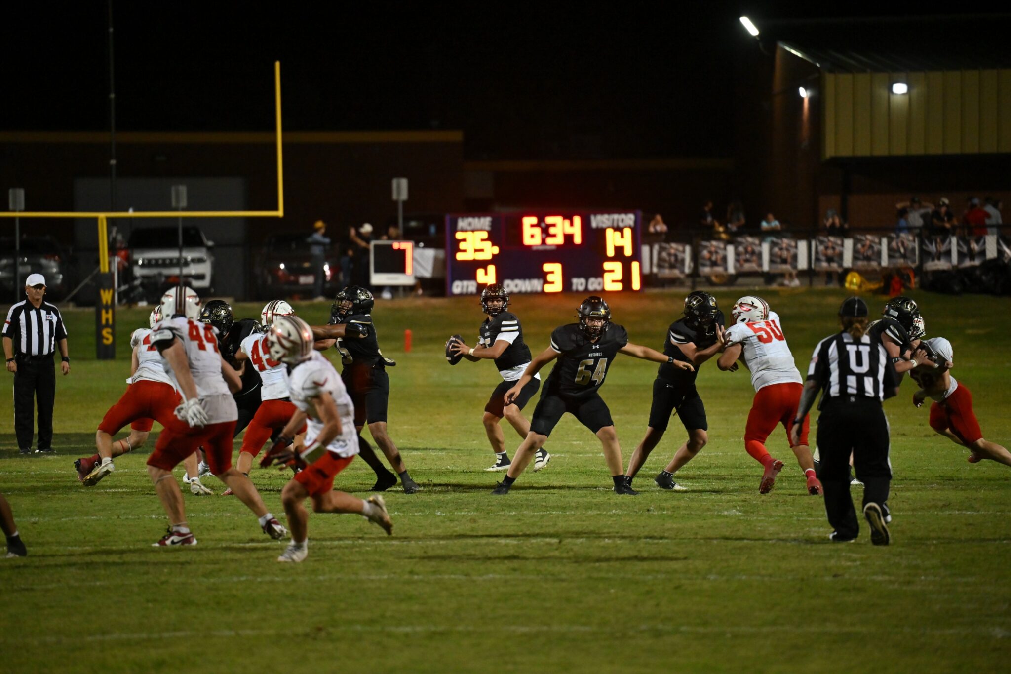 image13 1 | Press Pass Sports Nighttime football game scene with players in black and white uniforms on a grassy field and a lit scoreboard in the background.