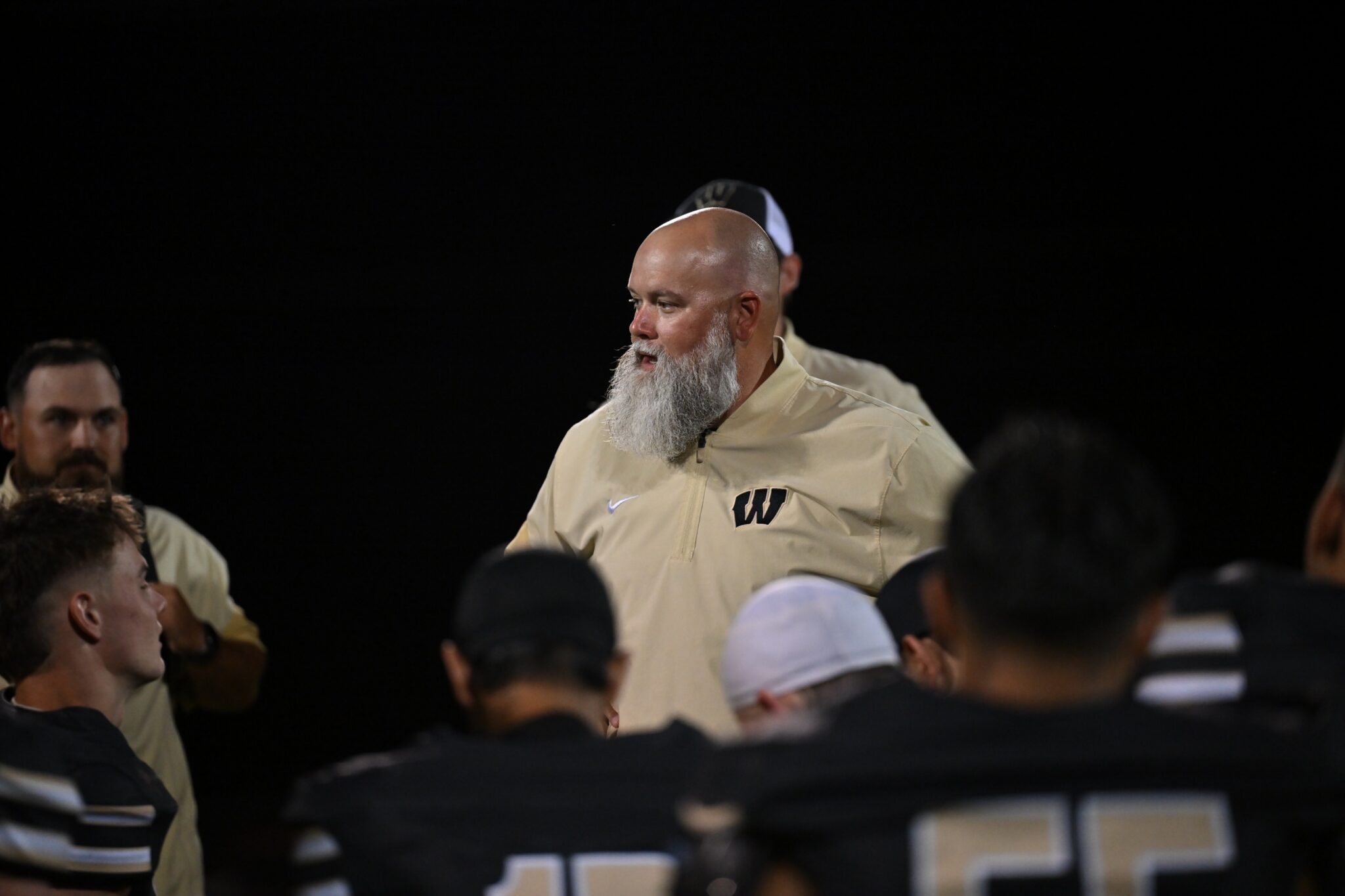 image16 | Press Pass Sports A bald man with a gray beard speaks to a crowd at night, wearing a beige jacket with a'W' logo.