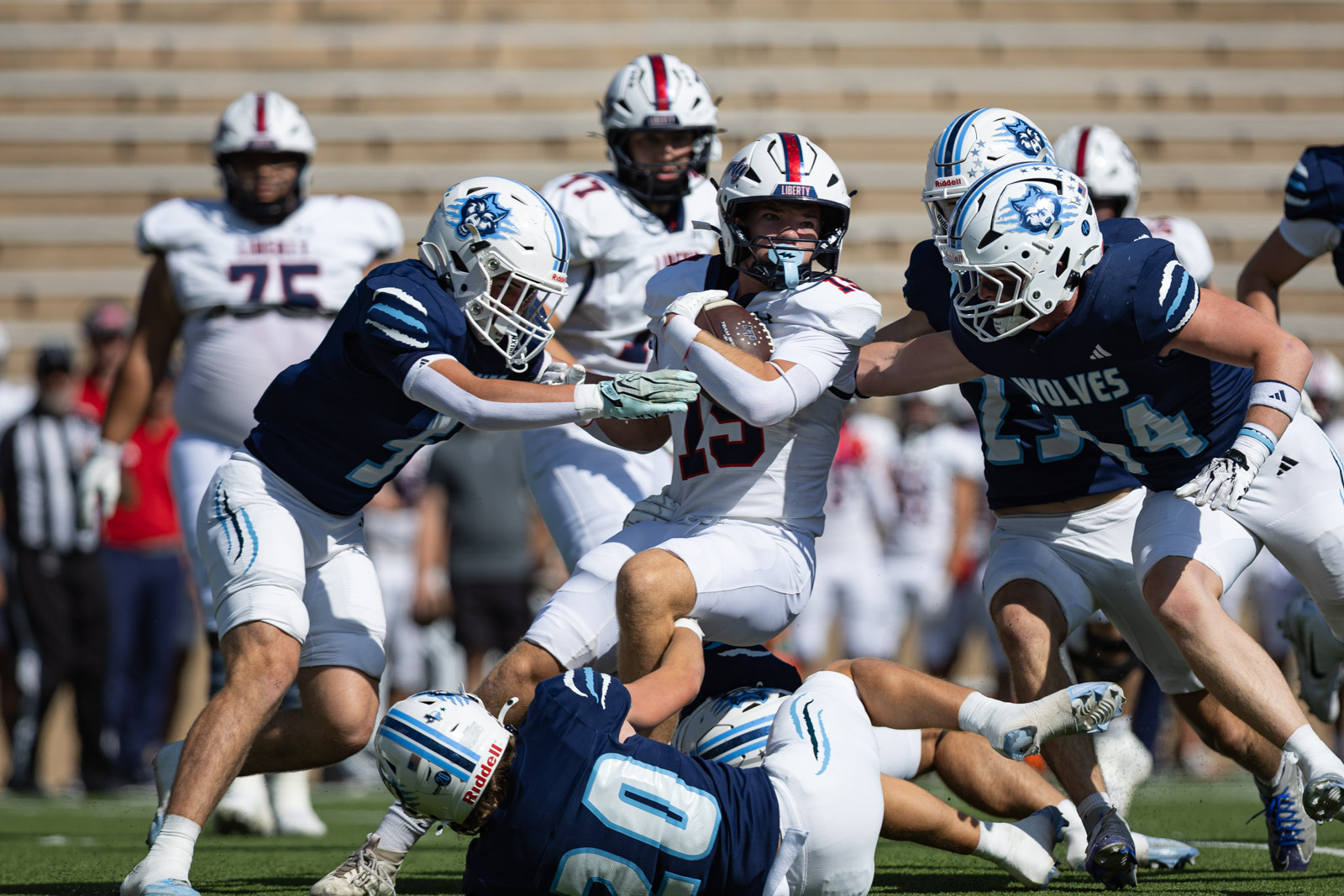 LHS-WPHS-FB-5 | Press Pass Sports Quarterback wearing number 15 in white, holding the ball as a defender in navy tackles him during a daytime football game.