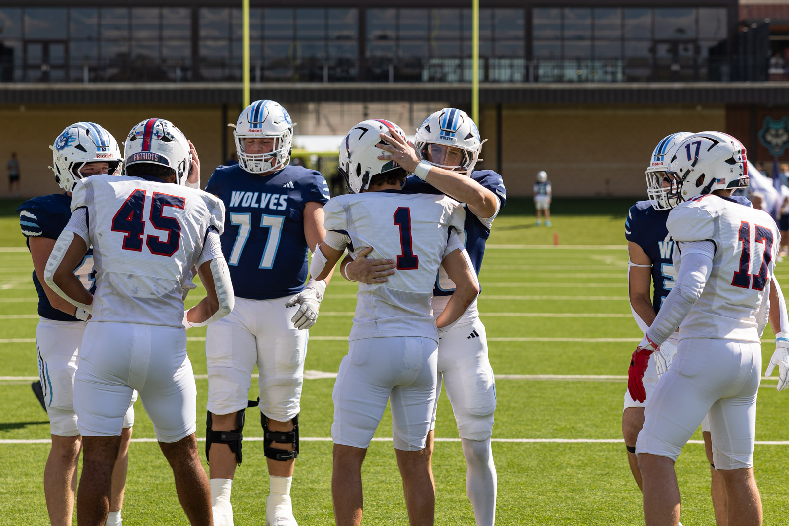 LHS-WPHS-FB-10 | Press Pass Sports Football players in white and blue uniforms huddle on a sunny field during a game.