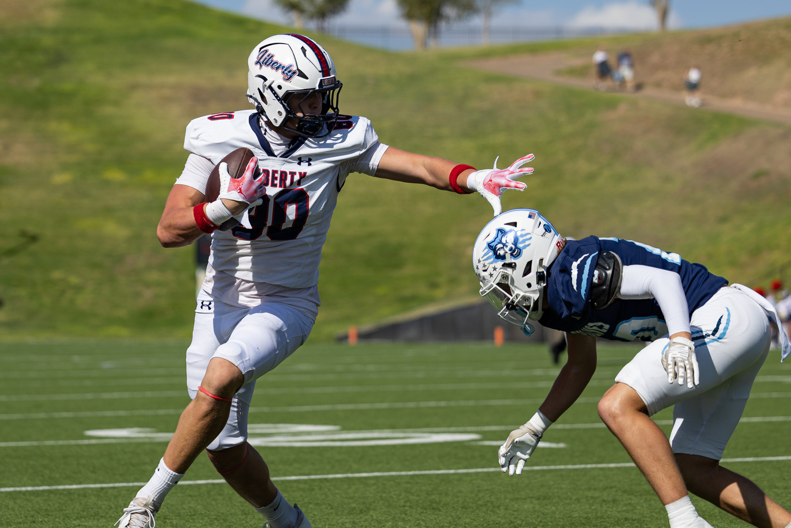 LHS-WPHS-FB-14 | Press Pass Sports Football game: white-uniformed runner (number 90) cradles the ball while a defender in blue halts him on a green turf field.