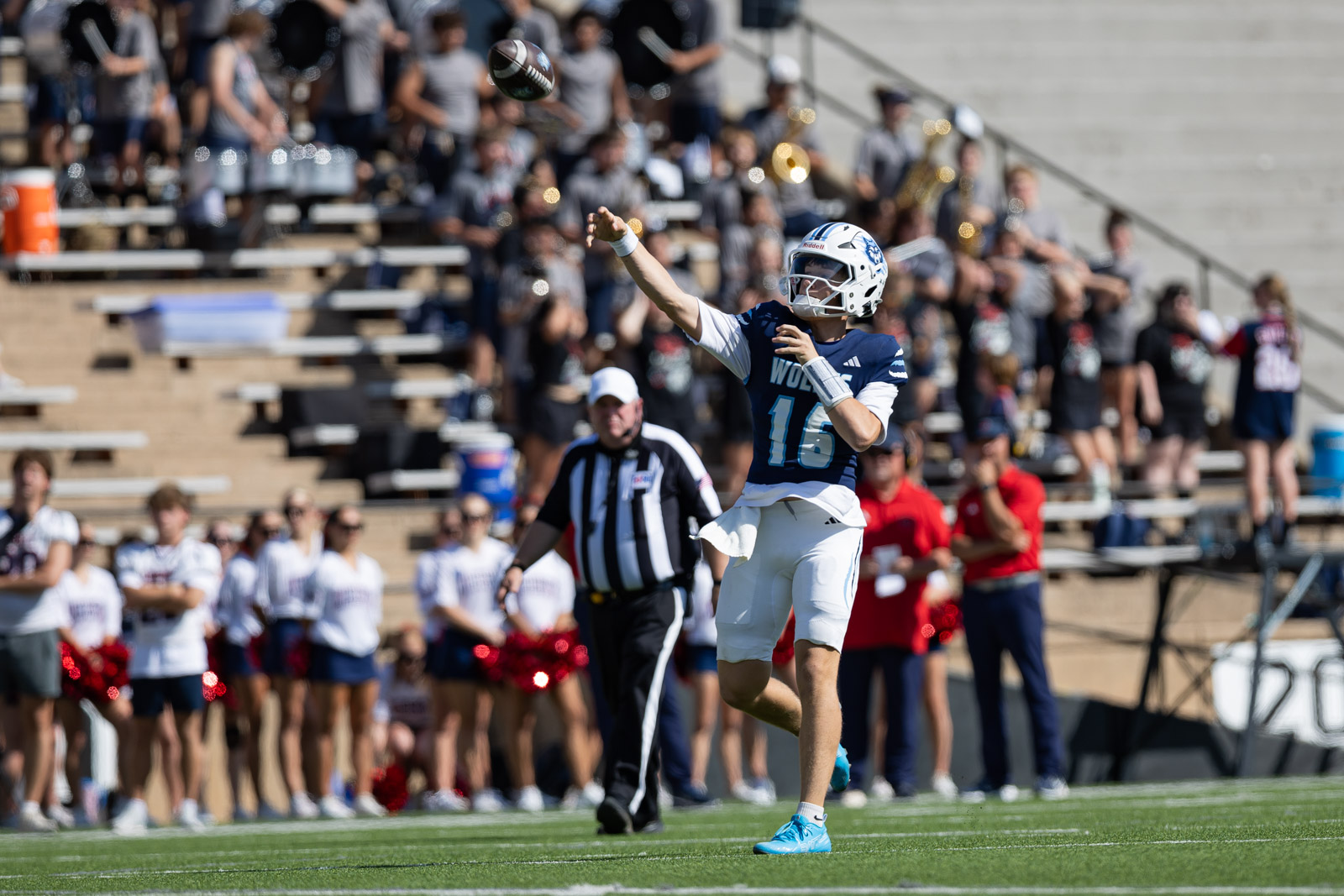LHS-WPHS-FB-16 | Press Pass Sports Football quarterback in blue and white uniform throws a pass, ball mid-air, as crowd and referee watch on a sunny sideline.