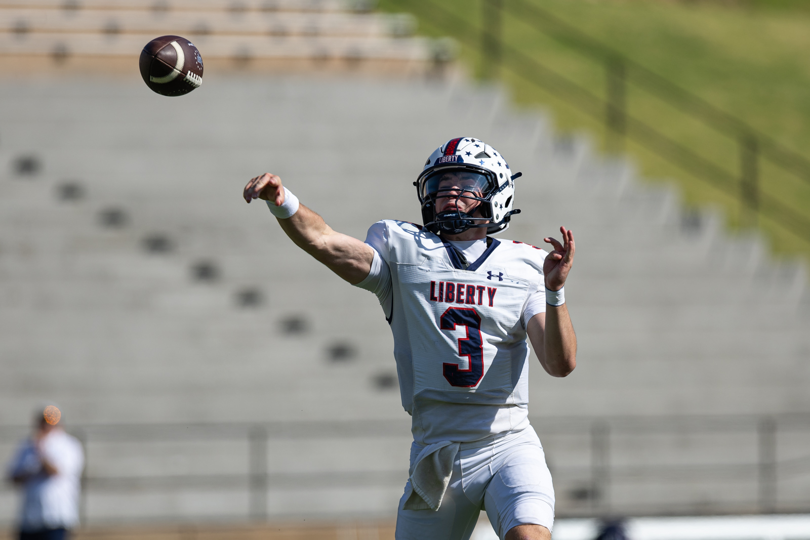 LHS-WPHS-FB-23 | Press Pass Sports Liberty quarterback wearing #3 in a white uniform throws a pass on a sunny football field, helmet on.