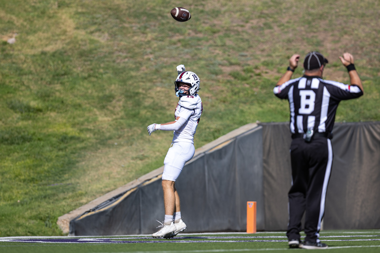 LHS-WPHS-FB-31 | Press Pass Sports Football player in white jersey leaps to catch a pass as the ball comes down, near the sideline with a striped referee raising arms nearby.
