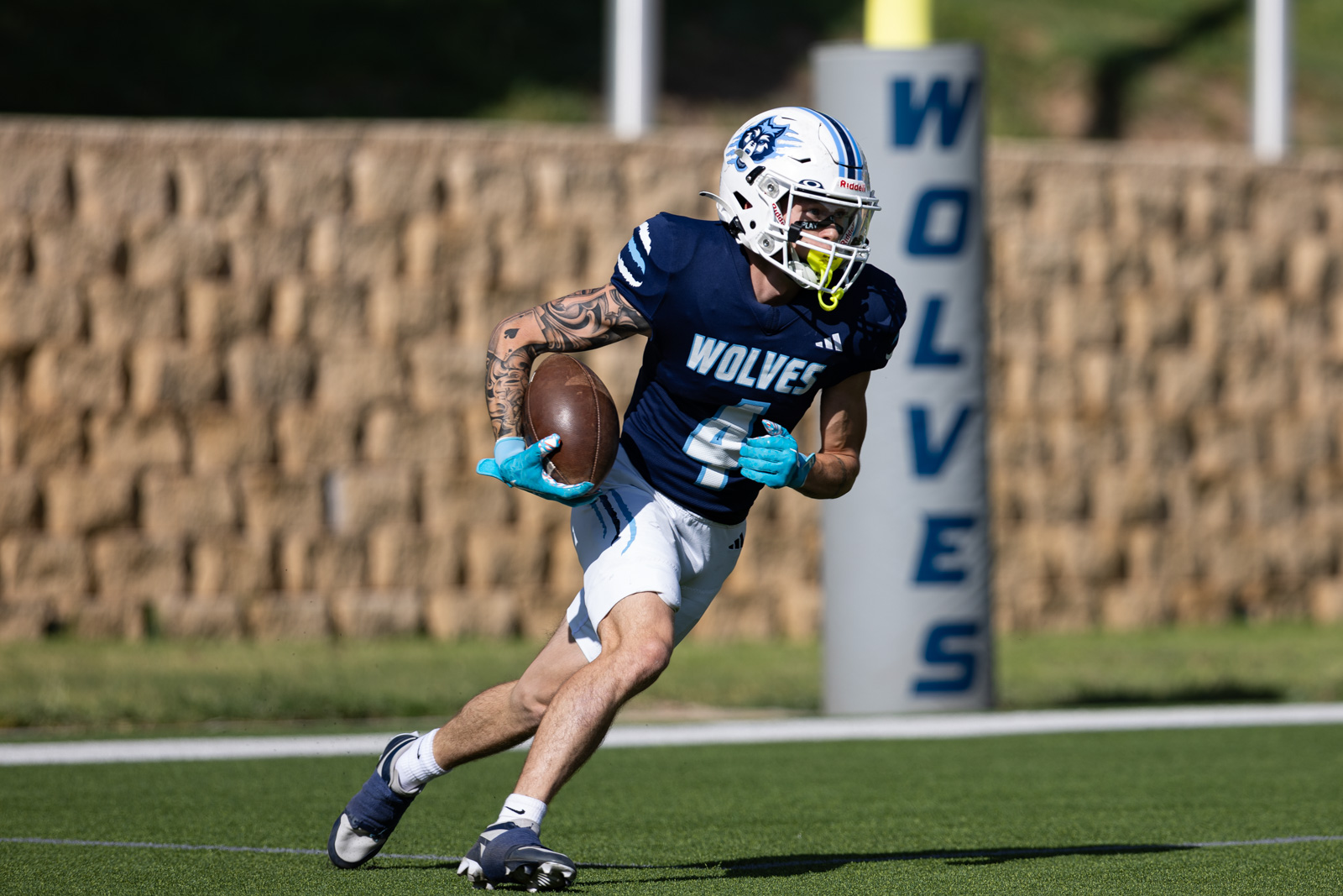 LHS-WPHS-FB-32 | Press Pass Sports Football player in a navy Wolves jersey running with the ball on a green stadium field, white helmet with a blue logo, blue gloves, and visible tattoos on the left arm.