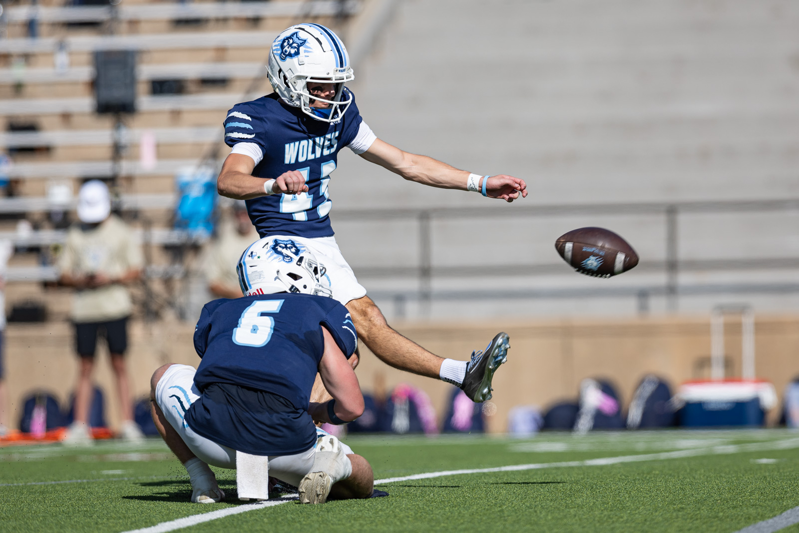 LHS-WPHS-FB-37 | Press Pass Sports Wolves football player #12 leaps midair over a teammate while a football sails nearby on the field.