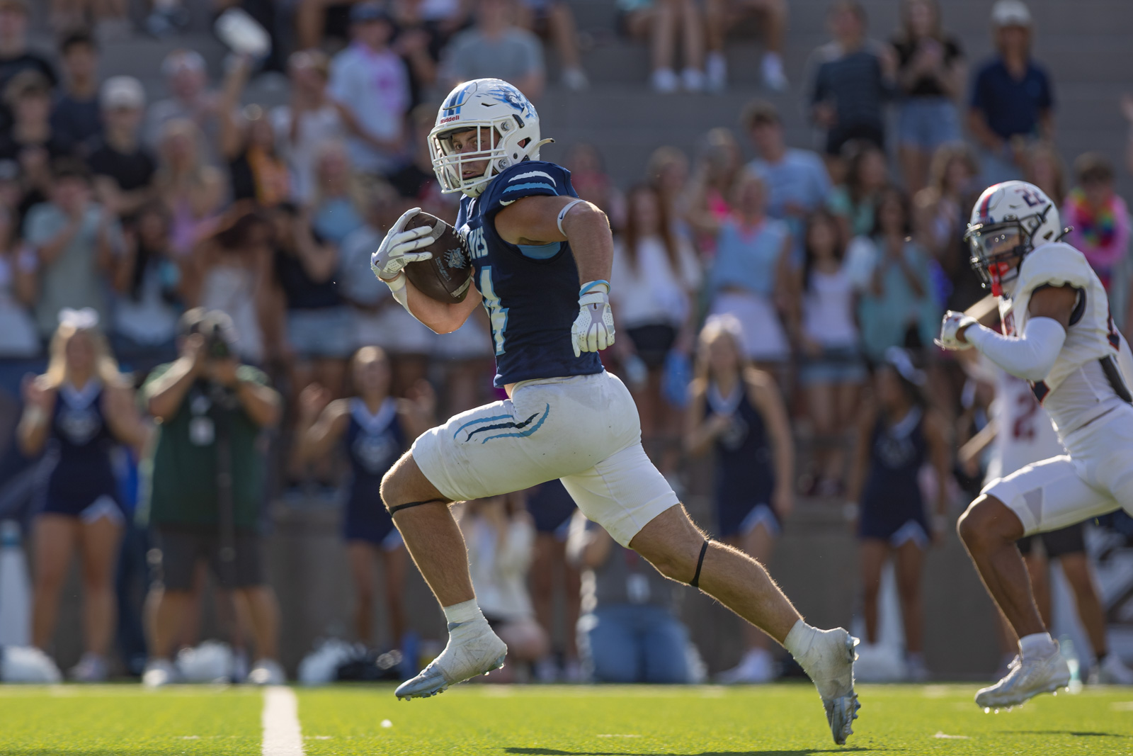 LHS-WPHS-FB-43 | Press Pass Sports Football player in a blue jersey and white helmet runs with the ball during a game, crowd cheering in the background.