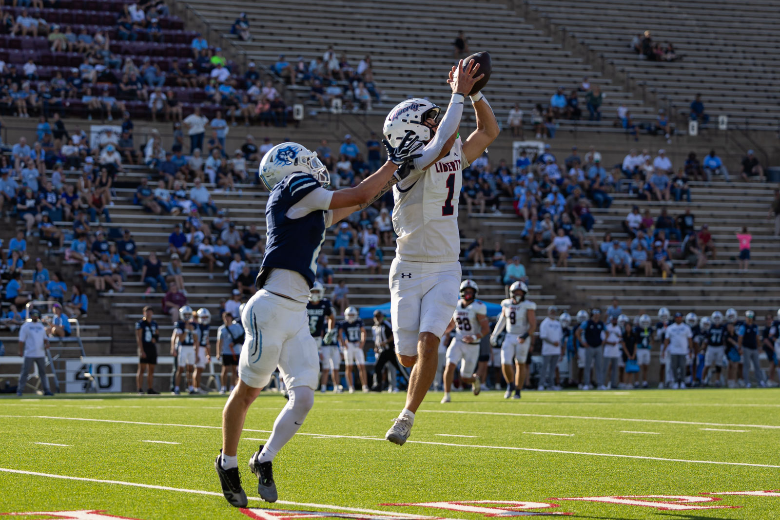 LHS-WPHS-FB-46 | Press Pass Sports Two football players jump for a tipped pass as the crowd watches from the stands on a sunny day.