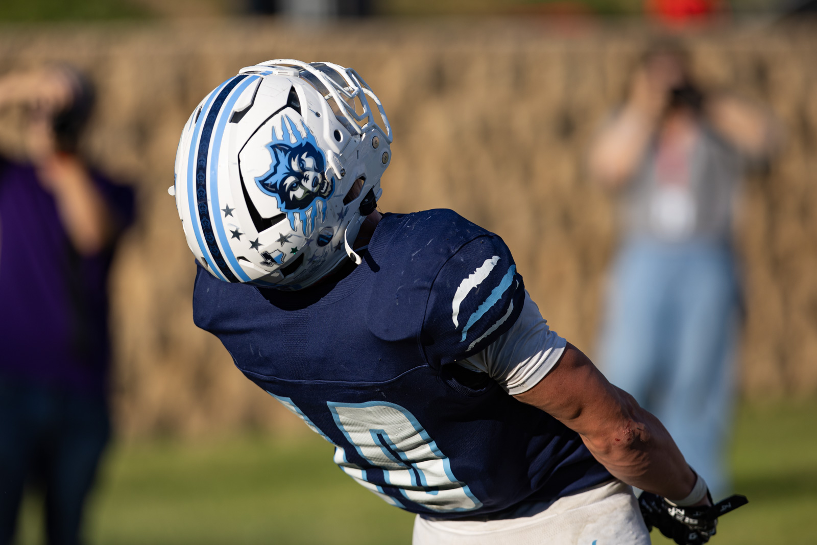 LHS-WPHS-FB-51 | Press Pass Sports American football player in a navy blue jersey leaning forward during a play, wearing a white helmet with a blue wolf logo.