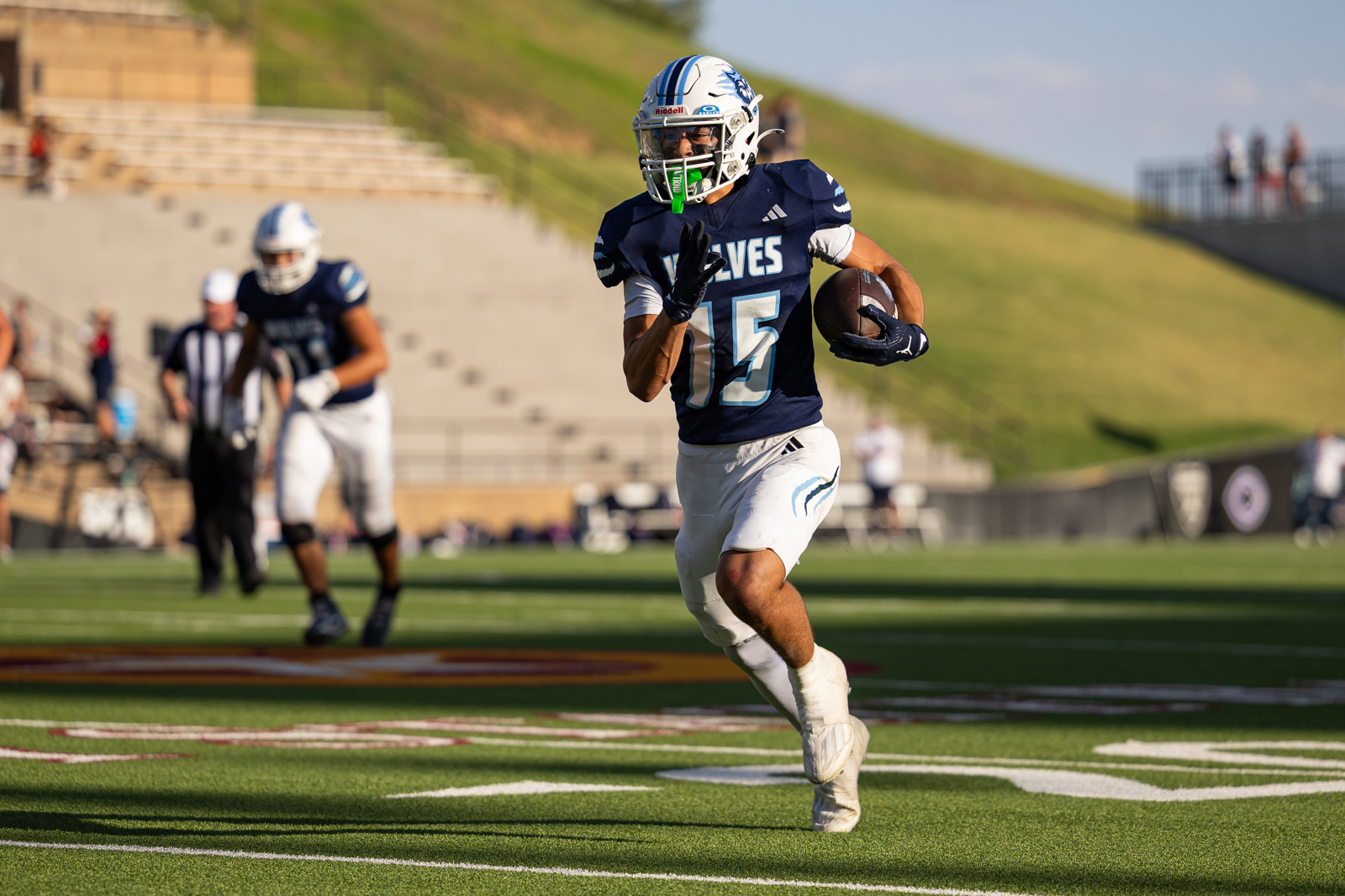LHS-WPHS-FB-53 | Press Pass Sports Football player in navy Wolves jersey, #15, running with the ball on a turf field during a game stadium background
