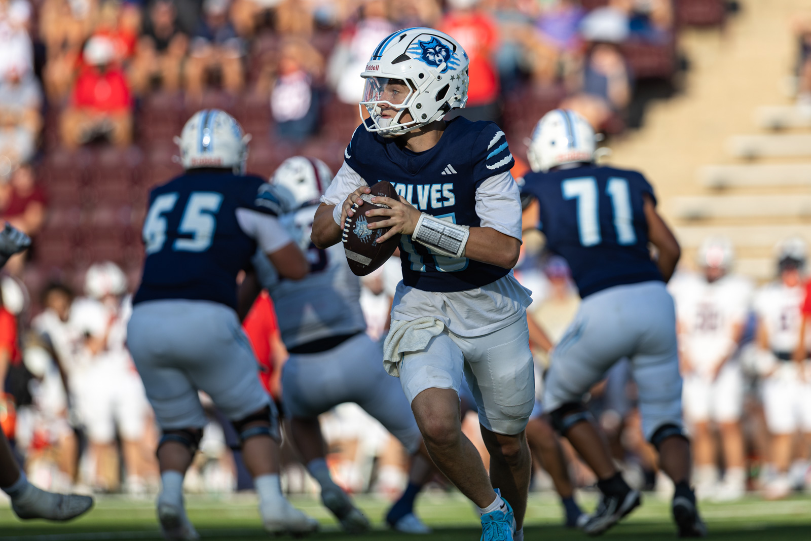 LHS-WPHS-FB-55 | Press Pass Sports Young football quarterback in navy Wolves jersey drops back to pass, gripping the ball, field crowd in background
