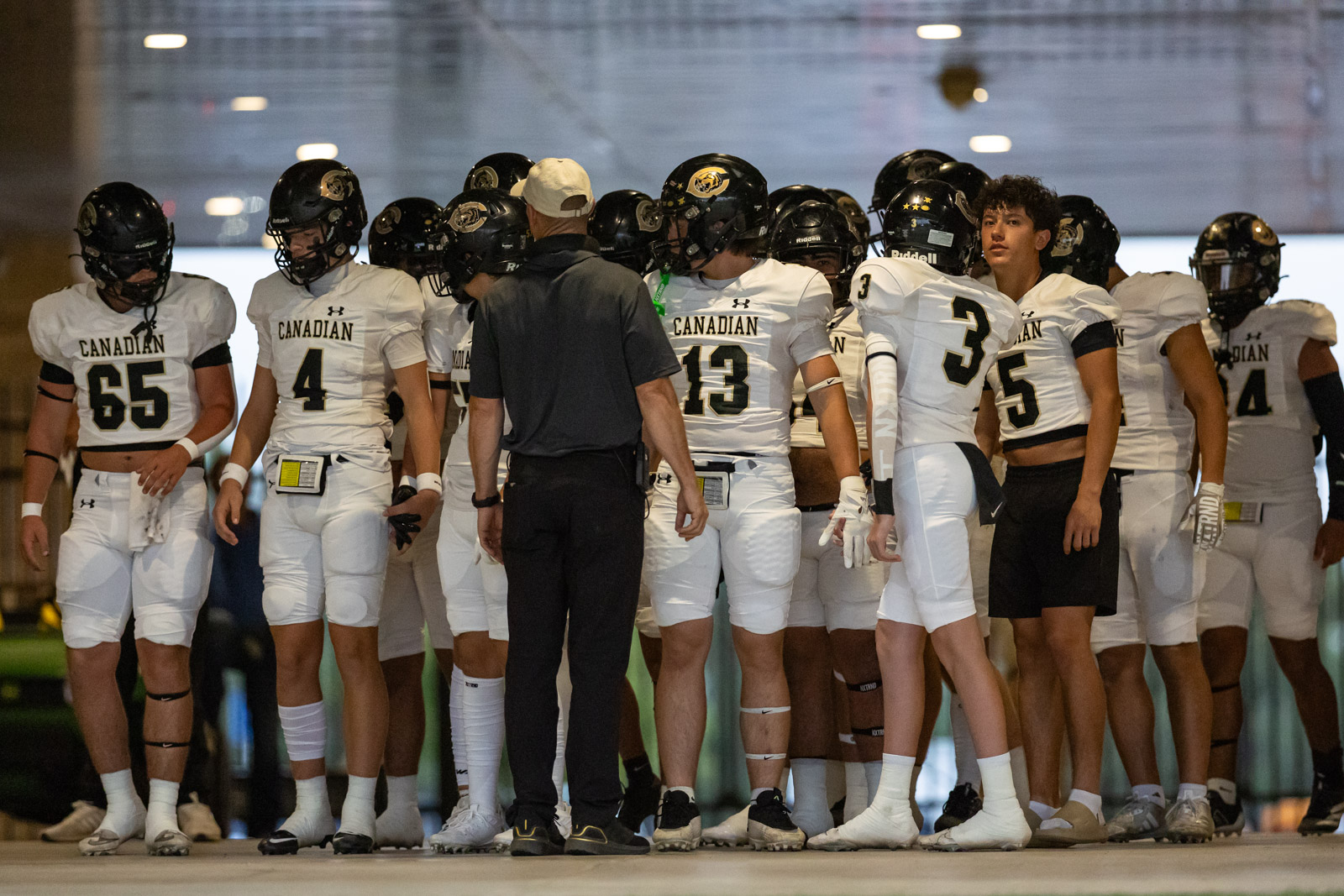 CHS-RHS-FB-1 | Press Pass Sports Canadian football players in white uniforms form a huddle around a coach in a black shirt on an indoor field.