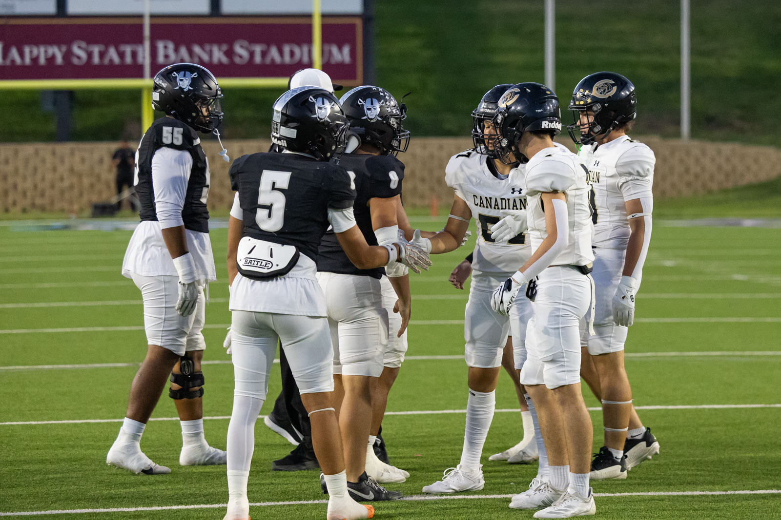 CHS-RHS-FB-3 | Press Pass Sports Football players in black and white uniforms exchange a handshake at midfield on a green turf field after a game, signifying sportsmanship.