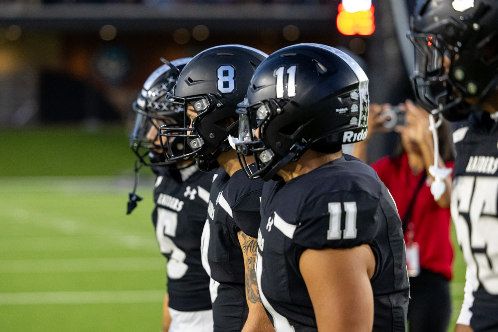 CHS-RHS-FB-4 | Press Pass Sports Line of football players in black uniforms standing on the sideline, helmets numbered 8 and 11 facing forward.