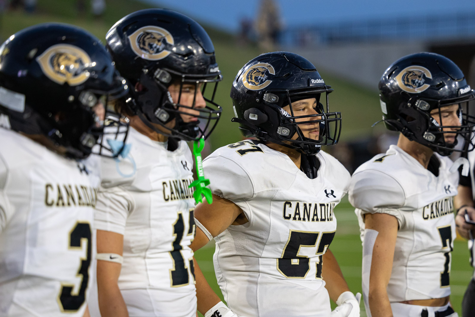 CHS-RHS-FB-5 | Press Pass Sports Canadian football players in white jerseys line up on the field, wearing black helmets with a gold emblem. (informative)