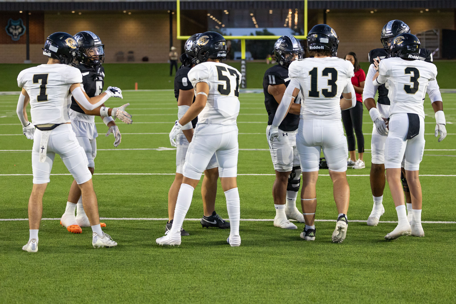 CHS-RHS-FB-6 | Press Pass Sports Football players in white uniforms huddle on a green turf field, preparing for a play before the game.