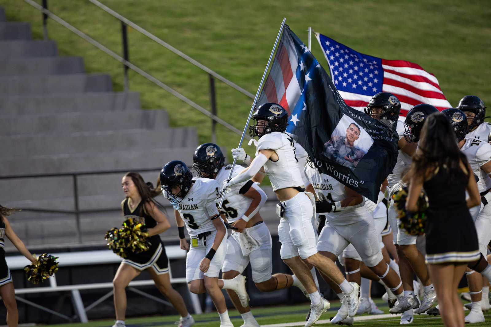 CHS-RHS-FB-8 | Press Pass Sports Football team in white uniforms runs onto the field as they carry flags, including an American flag and a memorial banner with a photo.