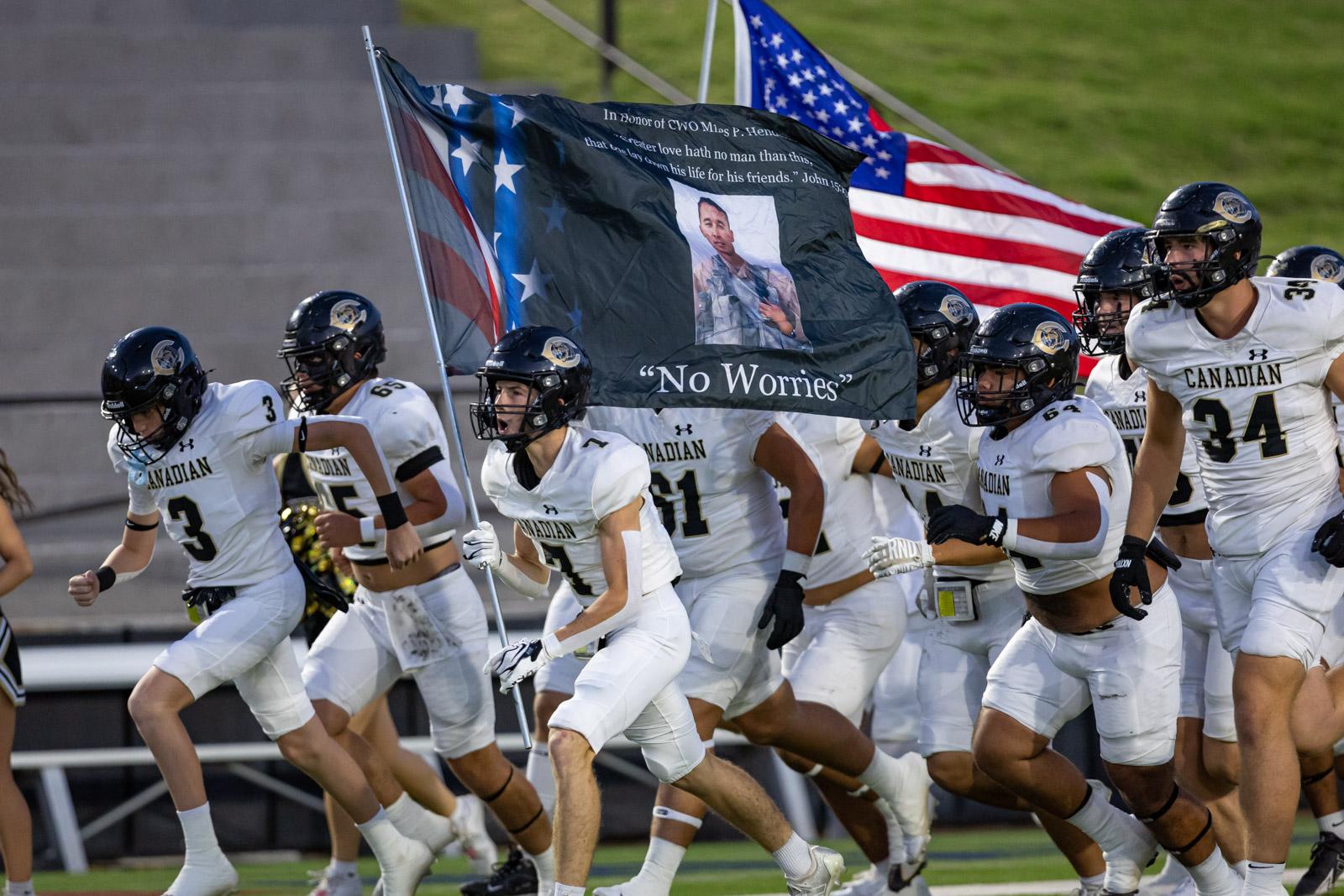 CHS-RHS-FB-9 | Press Pass Sports Canadian football players in white uniforms run onto the field under a large banner as the American flag waves in the background.