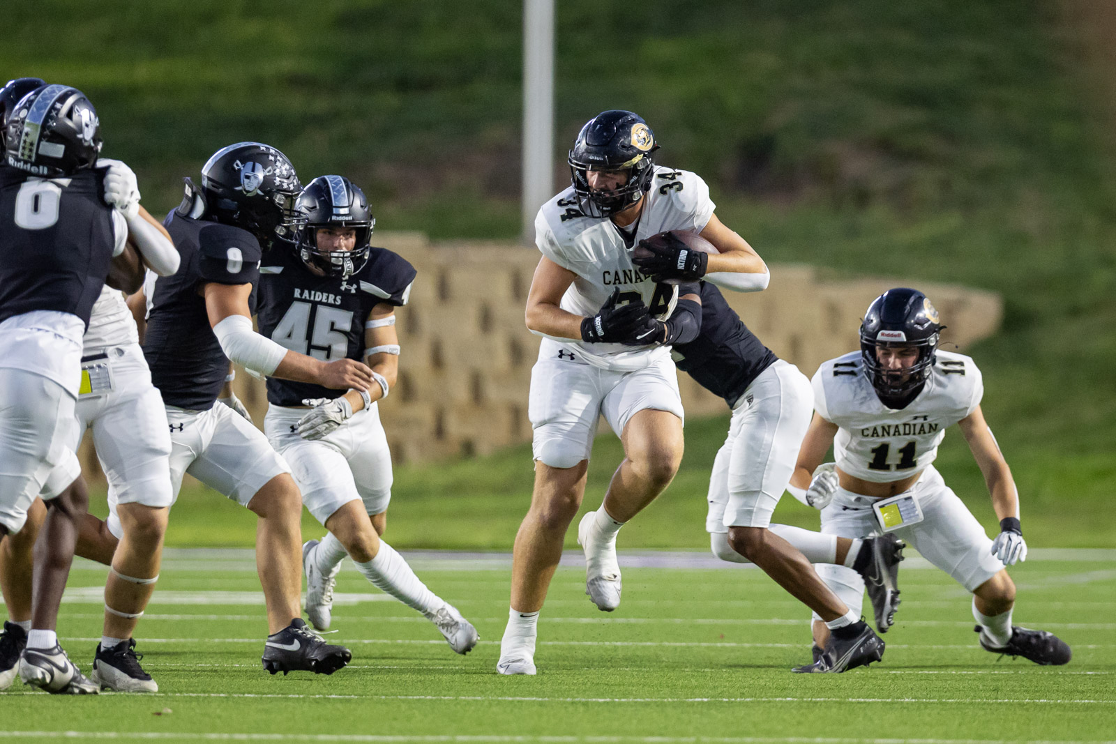 CHS-RHS-FB-12 | Press Pass Sports Football game action: a Canadian team player in white uniform runs with the ball as defenders in dark uniforms close in on a green turf field.