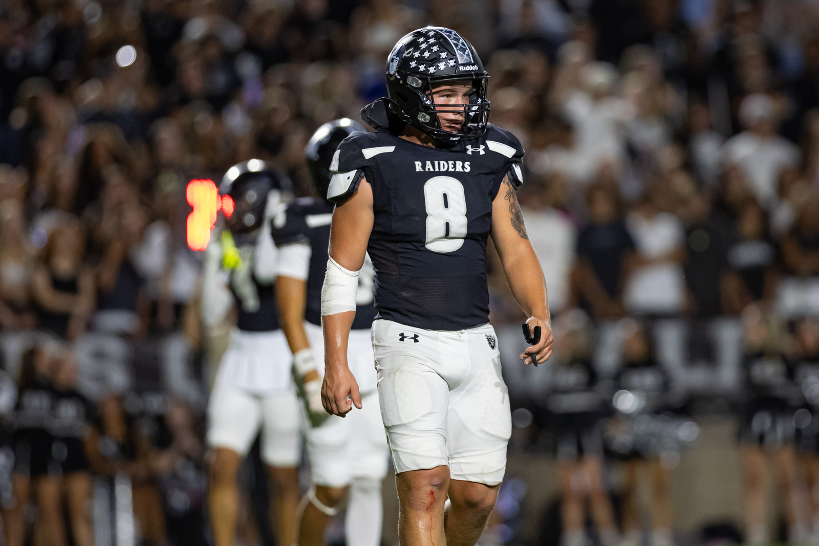 CHS-RHS-FB-19 | Press Pass Sports Raiders football player wearing number 8 in black jersey and white pants on the field with a cheering crowd in the background