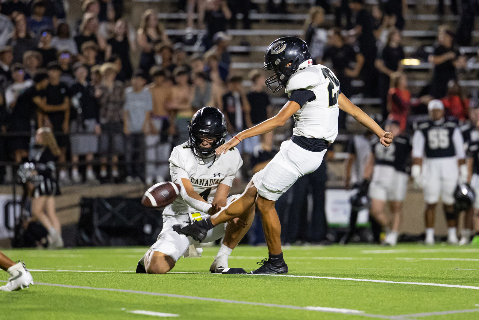 CHS-RHS-FB-22 | Press Pass Sports Canadian football players in white uniforms on a night game; one on the turf reaching for the ball while another leaps beside him, crowd in stands behind.