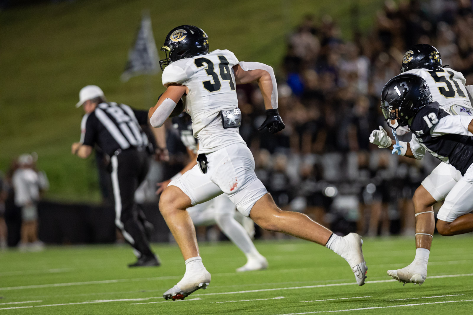 CHS-RHS-FB-24 | Press Pass Sports Football player in white jersey (#34) runs with ball on a green field, pursued by opponents under stadium lights, crowd in background.