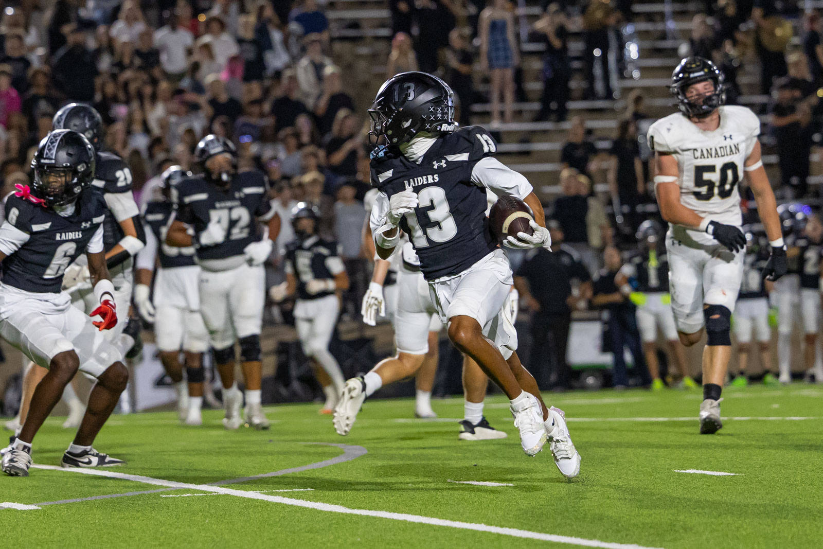 CHS-RHS-FB-28 | Press Pass Sports Raiders running back (#13) sprinting with the ball during a nighttime football game, crowd in the stands behind him.