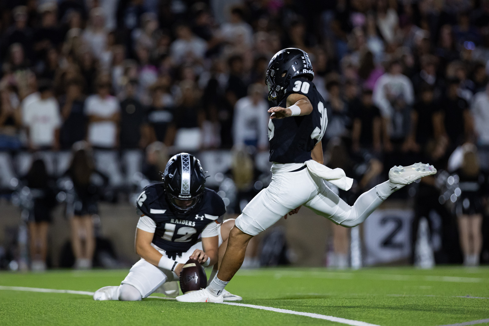 CHS-RHS-FB-29 | Press Pass Sports Football play: a navy jersey player wearing #30 jumps over a teammate on the ground (#12) near the loose ball on the turf.