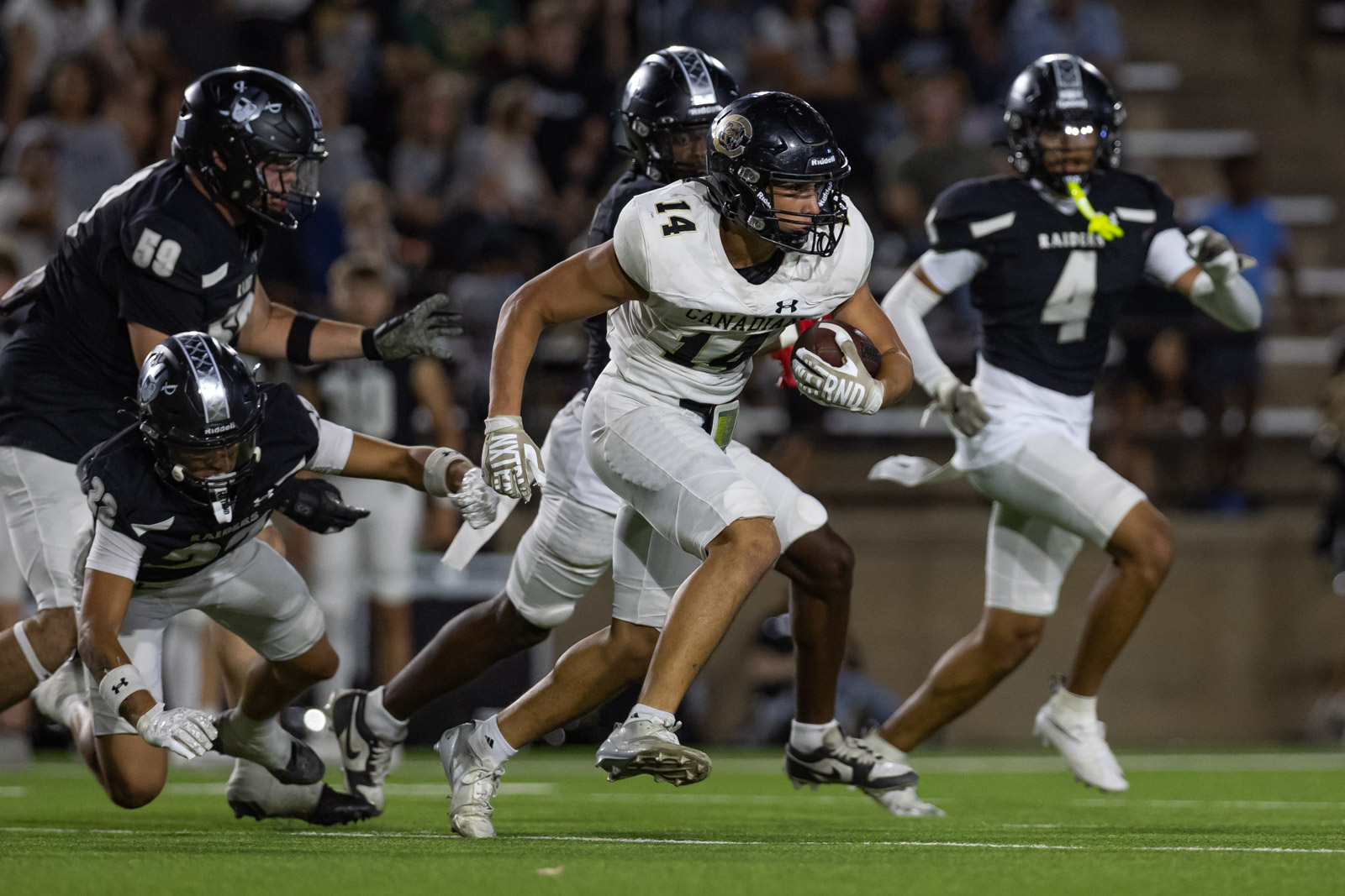 CHS-RHS-FB-33 | Press Pass Sports Canadian football player in white #14 sprints with the ball as black-uniform defenders close in on a green turf field at night stadium.