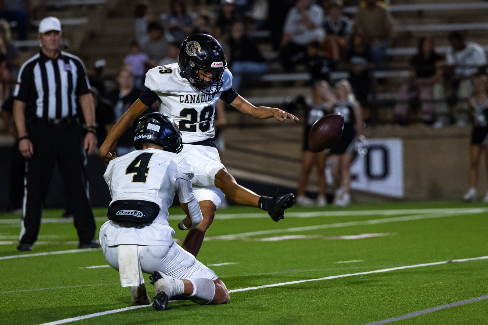 CHS-RHS-FB-36 | Press Pass Sports Two football players in white uniforms collide as a ball inches from the ground during a night game, with a referee in the background and a cheering crowd behind.