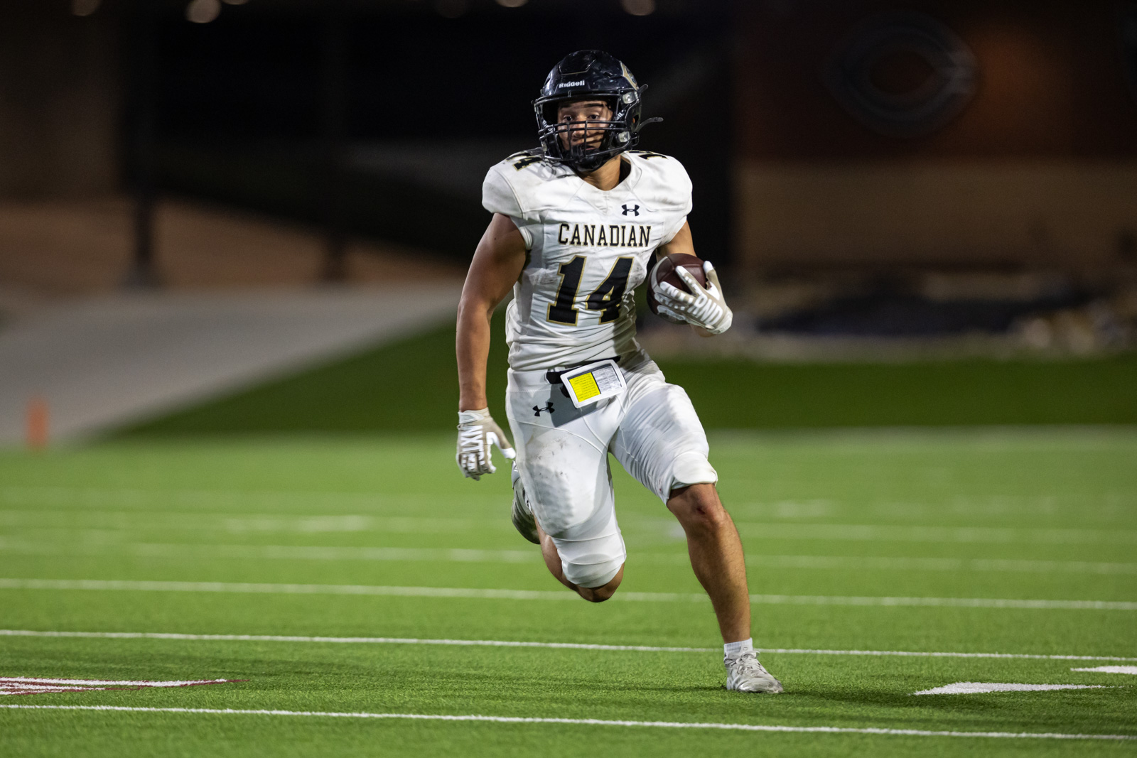 CHS-RHS-FB-39 | Press Pass Sports Canadian football player wearing number 14 in a white jersey runs with the ball on a green turf field at night, helmet on and gloves ready.